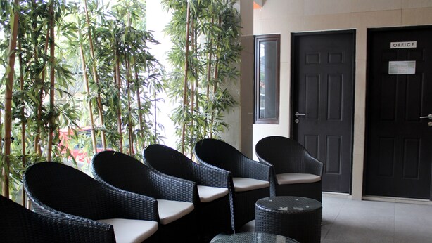 Un coin salon avec des fauteuils en osier et une table à plateau en verre, une porte portant l’inscription « BUREAU », et des plantes en bambou en arrière-plan.