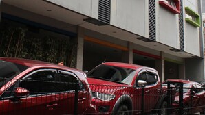 Un bâtiment moderne doté de nombreux balcons et d’un parking où sont garées des voitures rouges.