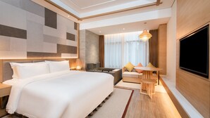 A modern hotel room with a large bed, a seating area with a table, a TV, and a large window with curtains. - Holiday Inn Resort Yichun Mingyue Mountain by IHG (Yichun)