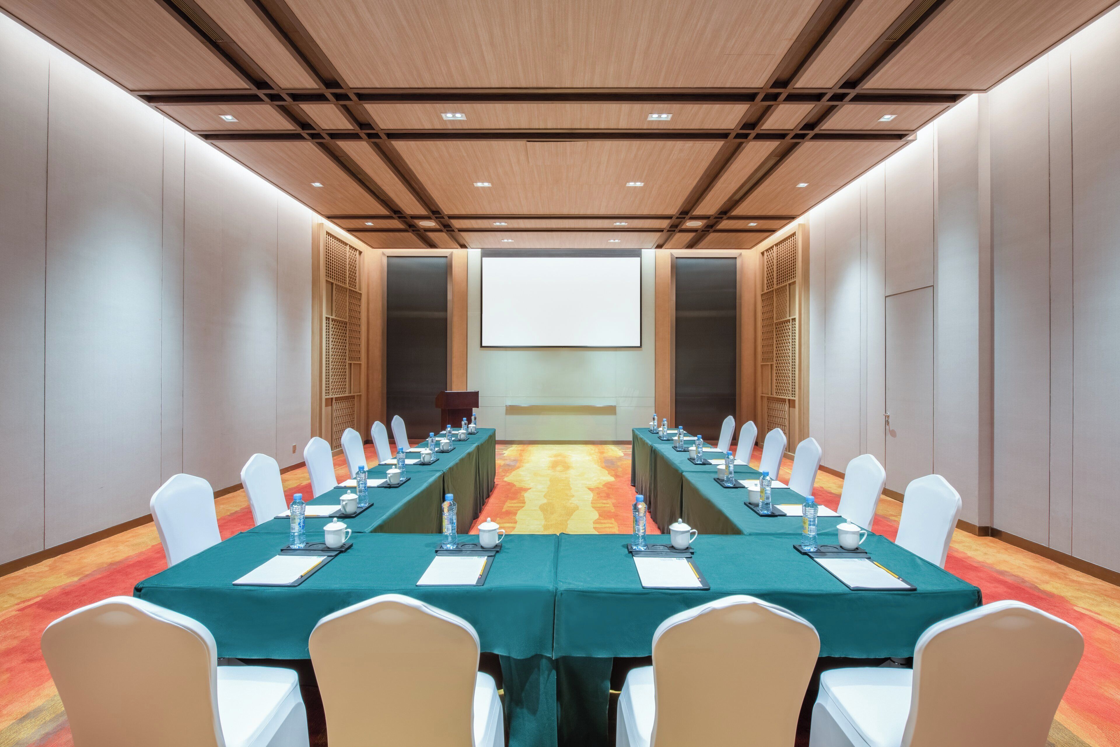 Un salón de conferencias con una larga mesa, sillas y una pantalla de proyector.