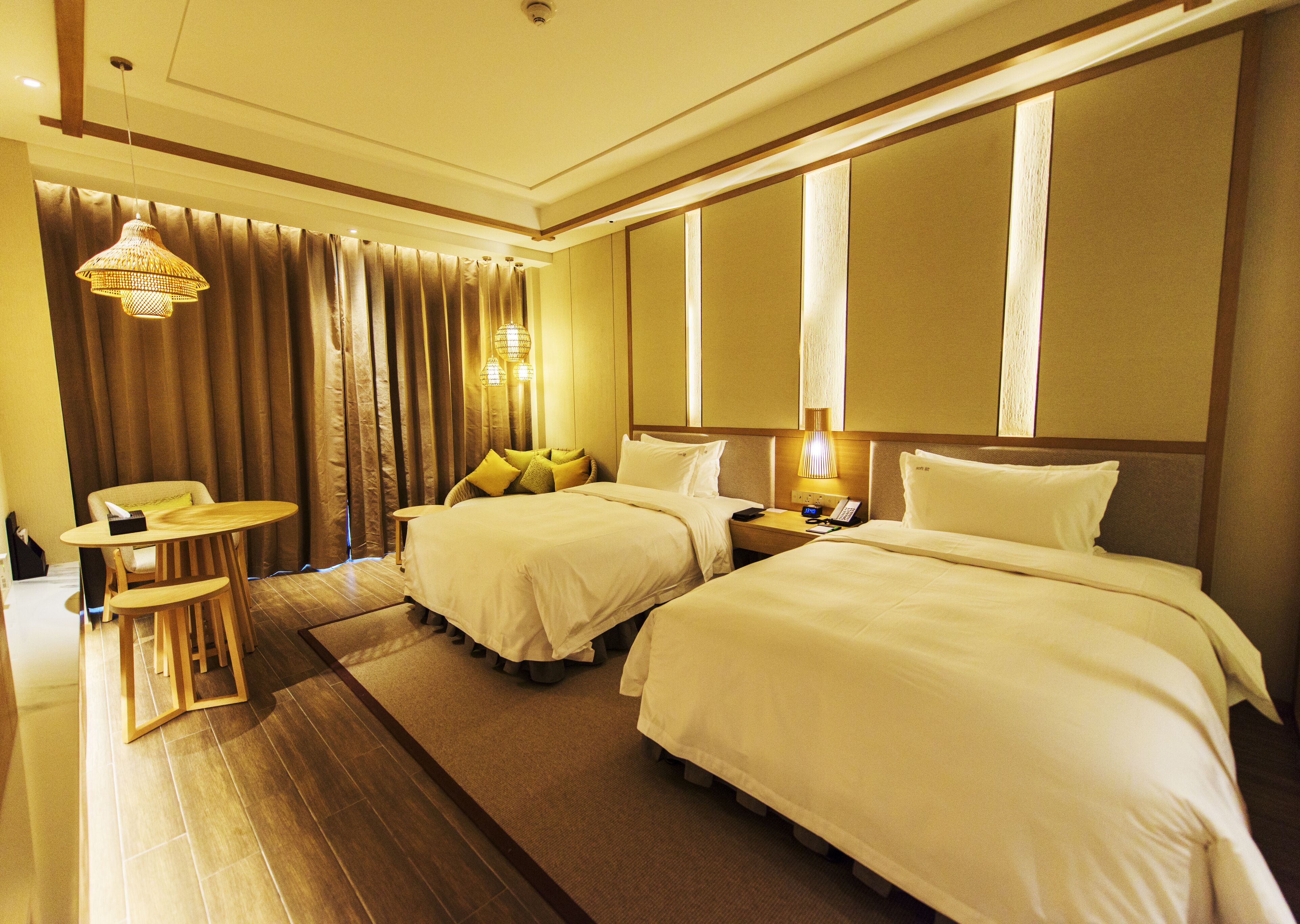 A hotel room with two beds, a small table, a chair, a lamp, and a curtain.
