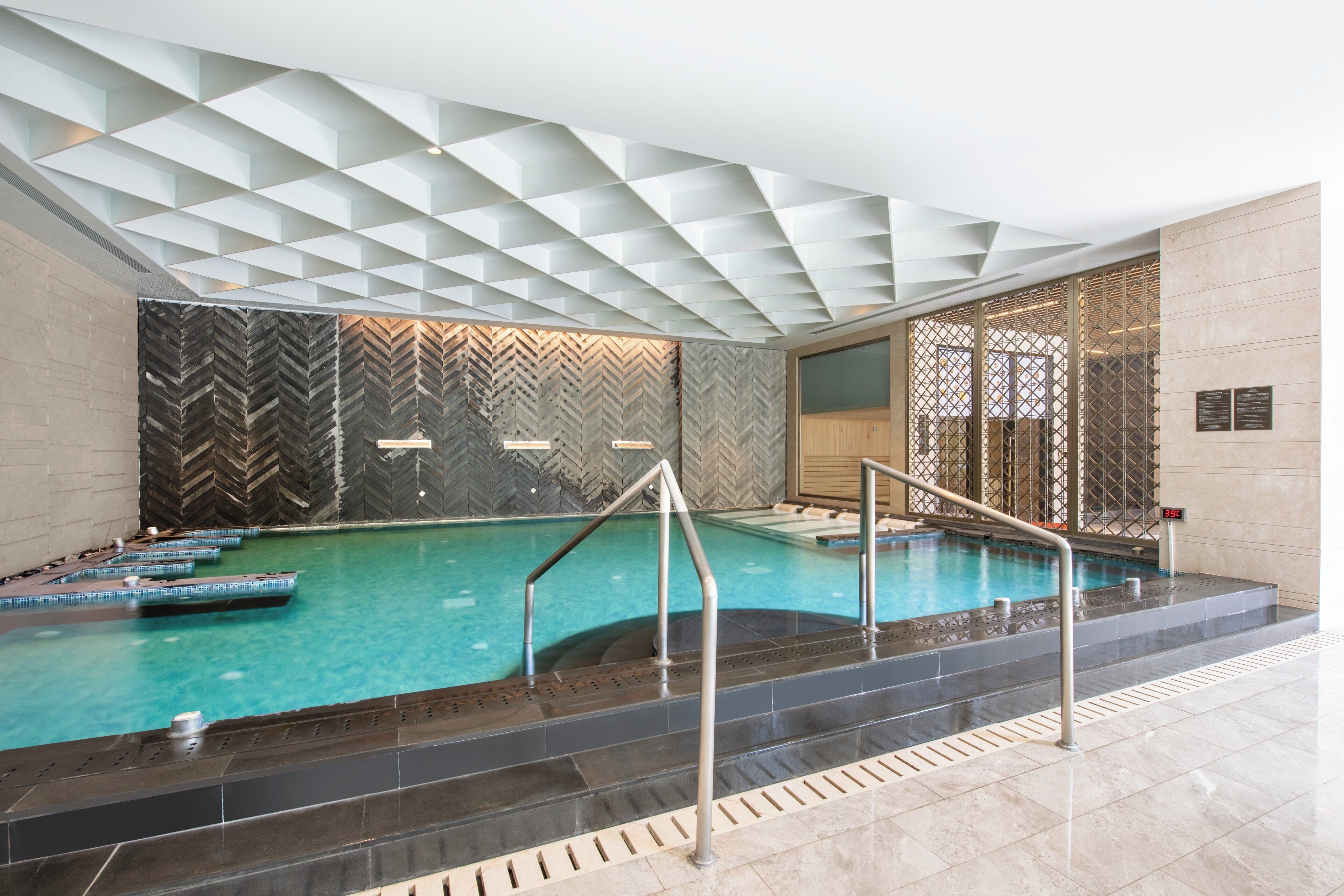 Una piscina interior con un diseño geométrico en el techo, una pared con motivo de espiga y un indicador de temperatura.