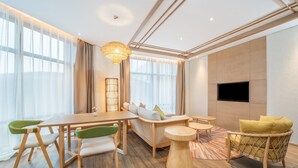 A modern living room with a wooden dining table, green and white chairs, a sofa with cushions, a patterned rug, and a television mounted on the wall. - Holiday Inn Resort Yichun Mingyue Mountain by IHG (Yichun)
