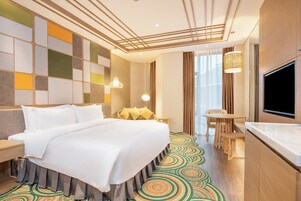 Habitación de hotel con una cama grande, televisor, una mesita y una alfombra estampada.