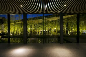 An indoor area with a modern design, featuring a glass wall that provides a view of a garden and a body of water outside. - THE MEIBIA MIYAZAKI (Miyazaki)