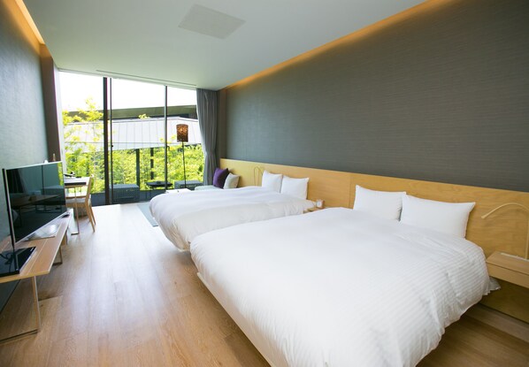 A modern hotel room with two beds, a desk with a flat-screen TV, and a large window offering a view of greenery. - THE MEIBIA MIYAZAKI (Miyazaki)