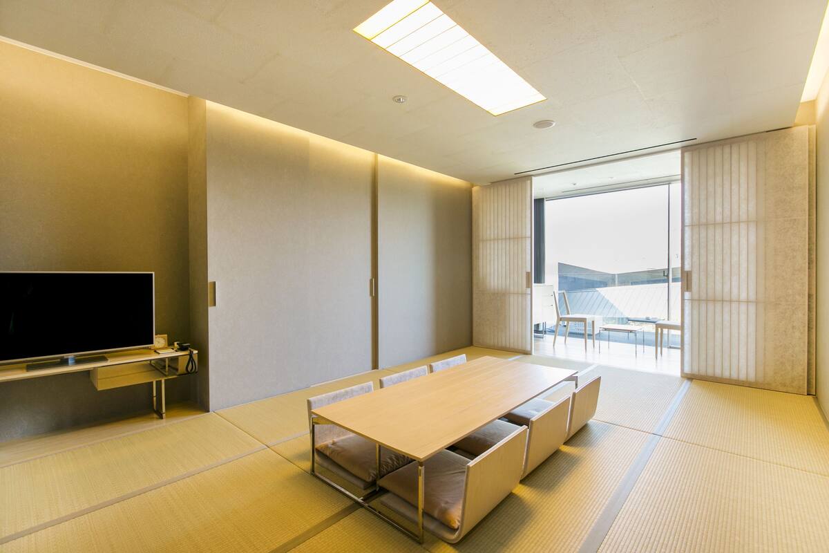 A modern conference room with a long table, chairs, a flat-screen TV, and large windows.