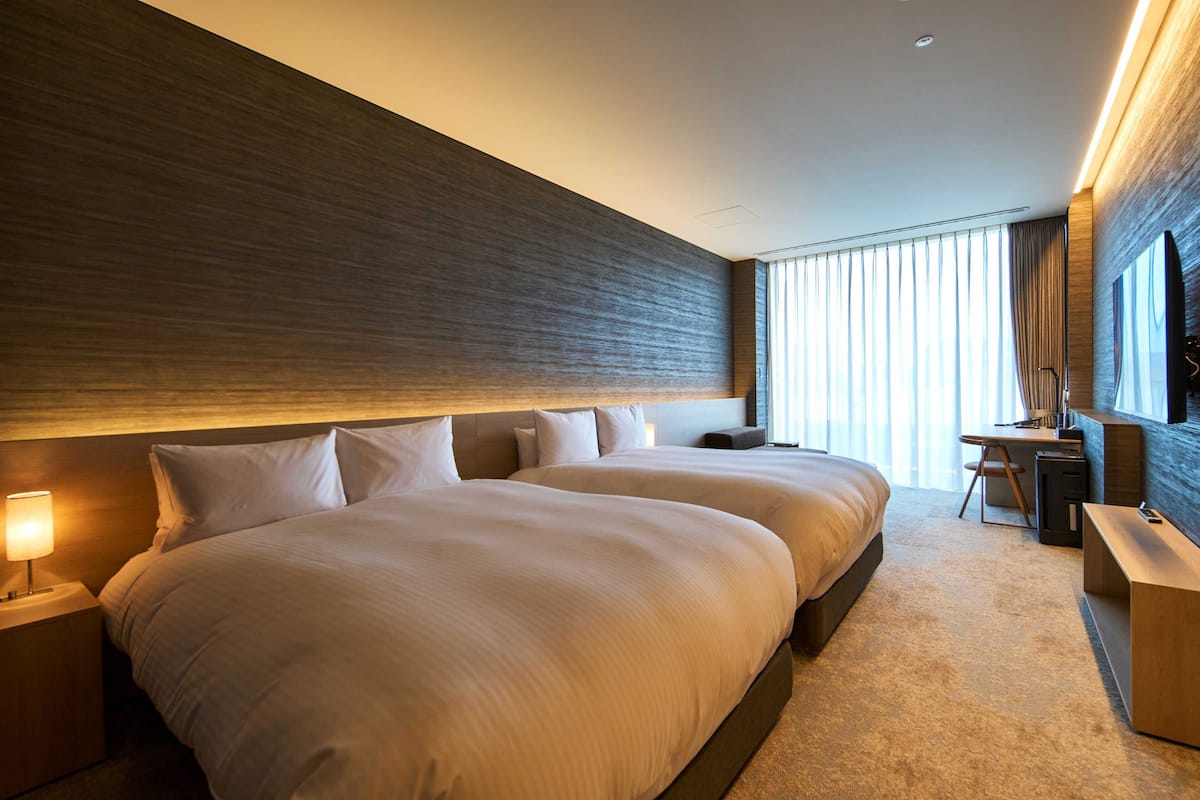 A modern hotel room with two large beds, a desk, a chair, and a television.