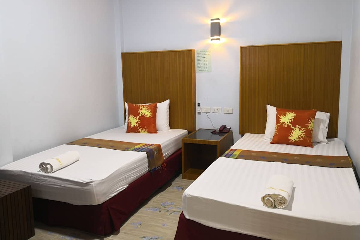 A hotel room with two single beds, each with a white mattress and red bedsheet, a wooden headboard, and a small bedside table with a phone.