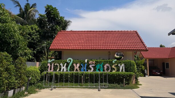 Un edificio con techo de tejas rojas, rodeado de vegetación y una valla metálica con letras coloridas.