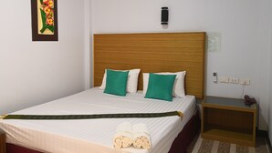 Una cama bien hecha con almohadas verdes y blancas, un cabecero de madera y una mesita de noche con un teléfono y una lámpara.