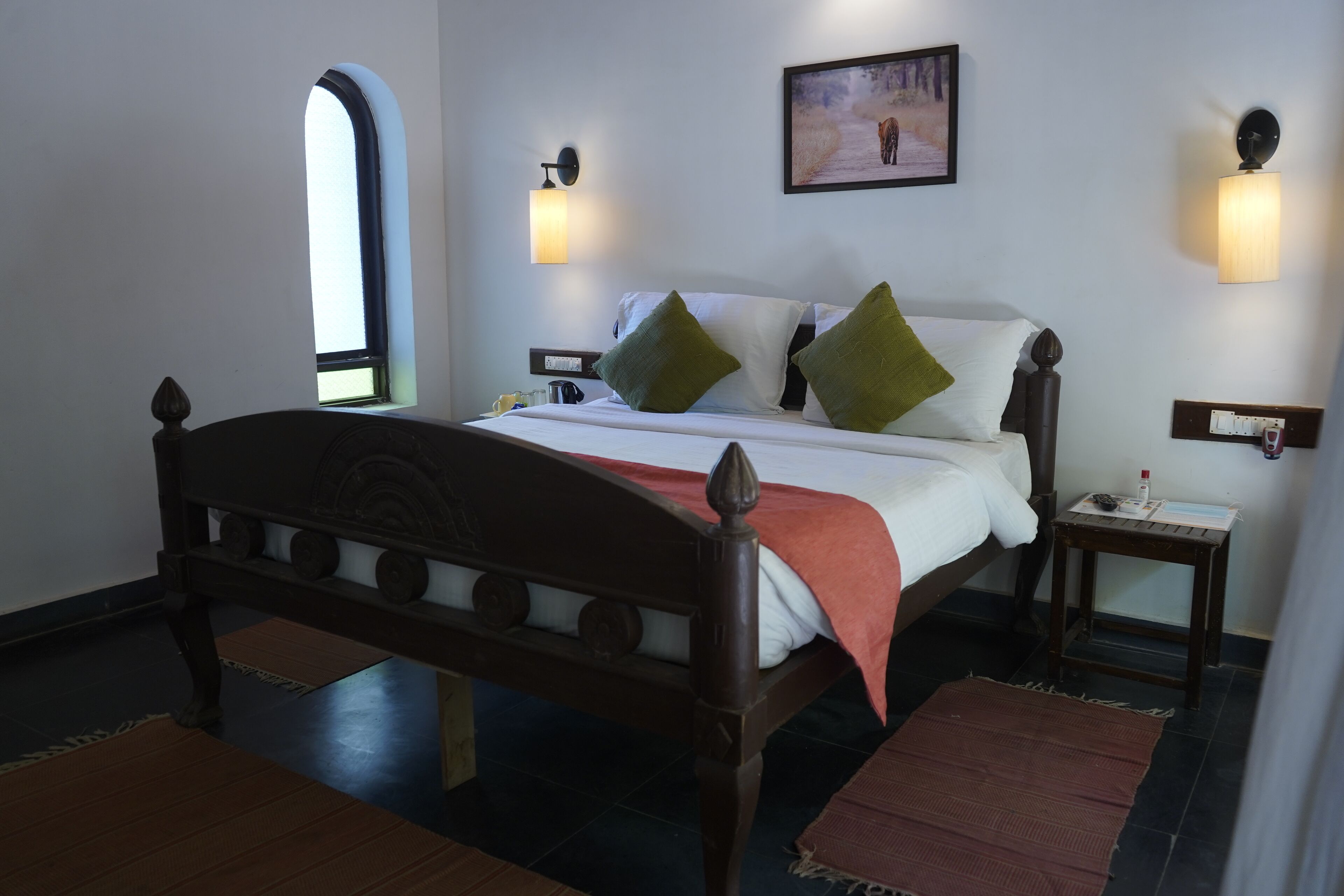 A bedroom with a wooden bed, two bedside tables, a nightstand, a window, and wall-mounted lights.