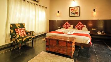 Quarto de hotel com cama, um baú de madeira, uma cadeira e uma mesa de cabeceira.