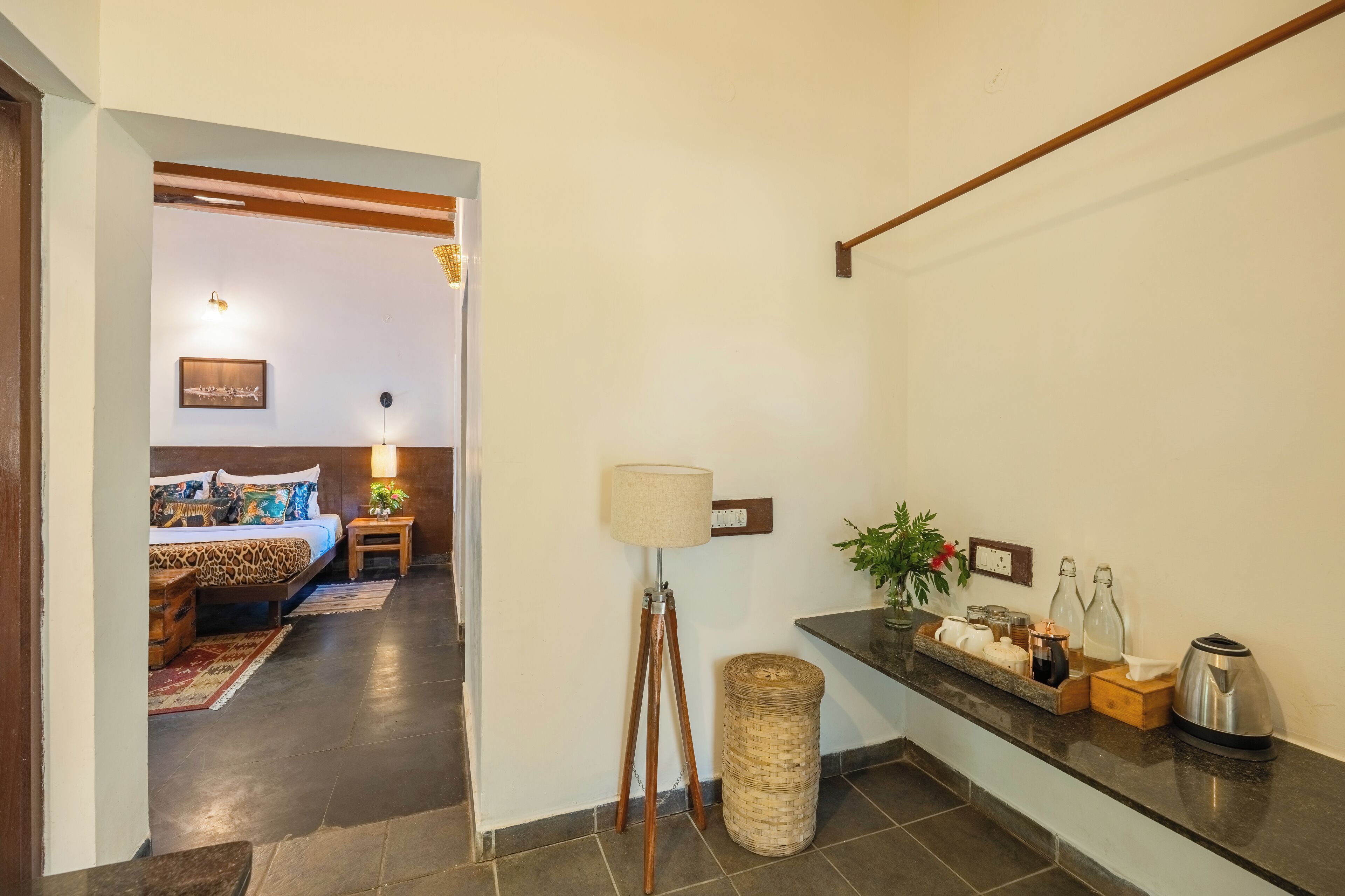 A hotel room with a bed, bedside table, lamp, and a small side table with a plant.