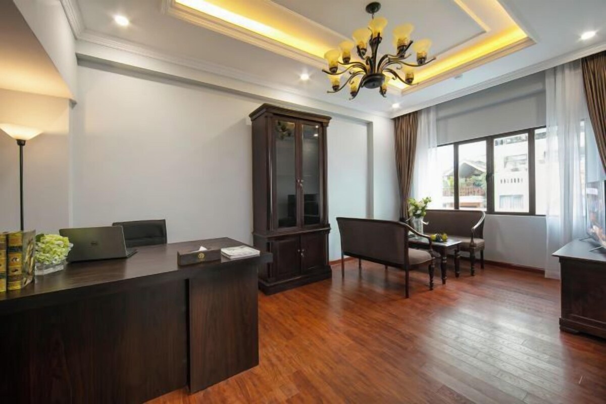 A hotel lobby with a reception desk, a large dark wooden cabinet, a chandelier, and a seating area with a sofa and chairs.