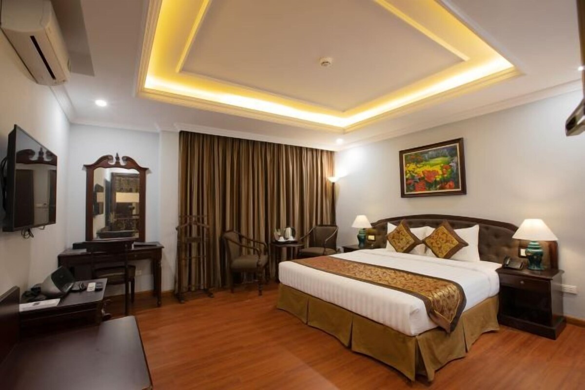 A hotel room with a large bed, a desk, a chair, a TV, and a painting on the wall.
