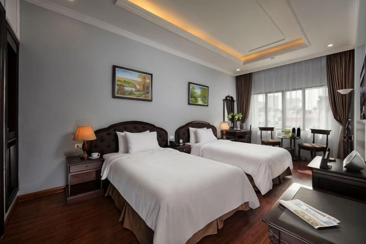 A hotel room with two beds, a desk, a chair, a lamp, and a window with curtains.