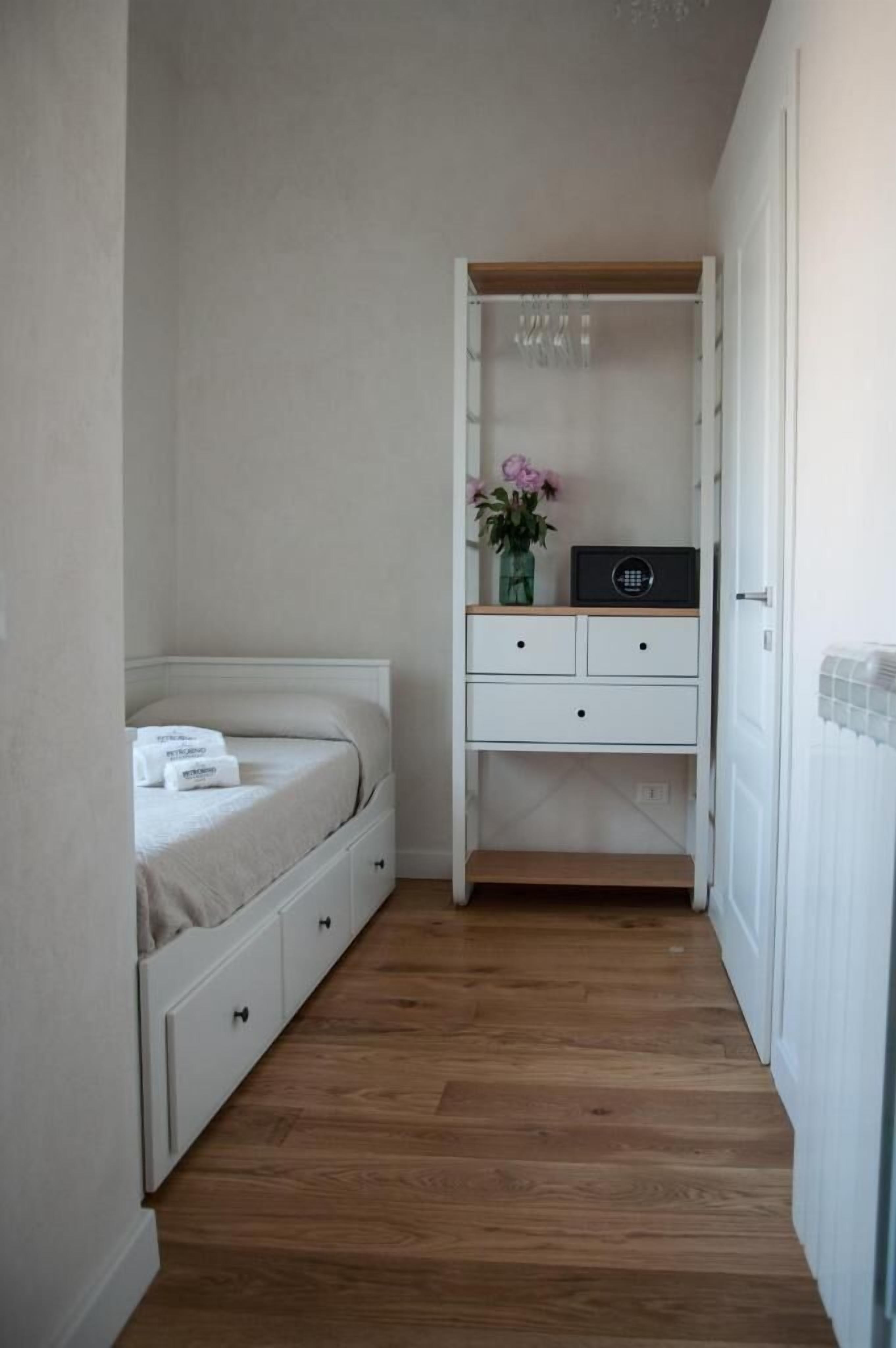 Une petite pièce comprenant un lit, une armoire blanche et une petite table sur laquelle est posé un vase de fleurs.