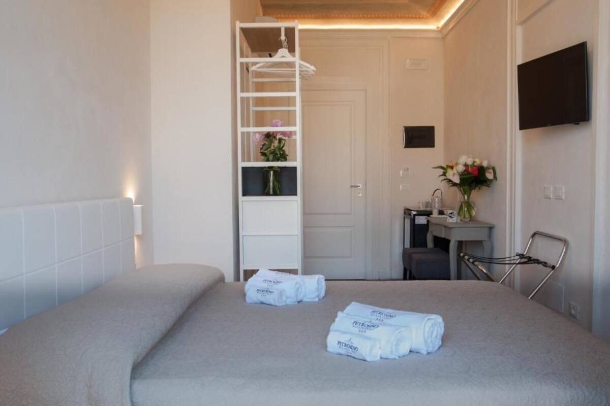 Een hotelkamer met een bed, een witte inbouwkast, een bureau met stoel, een televisie aan de muur en een klein plankje met bloemen.