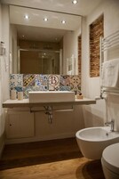 Un bagno con un lavandino bianco, un bidet e uno specchio. La parete presenta un motivo a mosaico e una parete decorata con mattoni.
