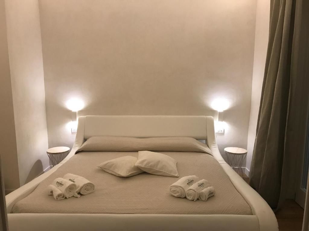 Cama bem arrumada com duas almofadas e toalhas enroladas, duas luminárias de cabeceira e uma cortina.