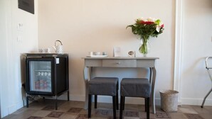 Una habitación pequeña con kitchenette, dos sillas, una mesa con un florero y un cubo de basura.