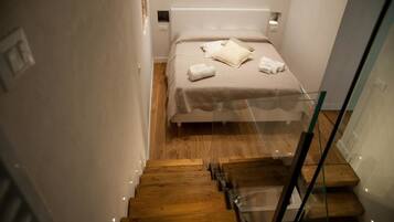 A bedroom with a bed, a glass railing, and a wooden staircase.