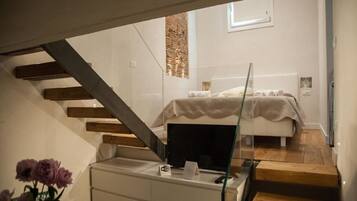 Un dormitorio moderno con una cama, un escritorio de cristal y una escalera que sube a un piso superior.