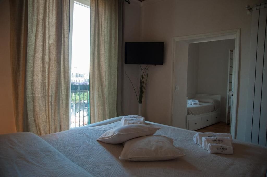 A hotel room with a bed, a TV mounted on the wall, a window with curtains, and a door leading to a bathroom.