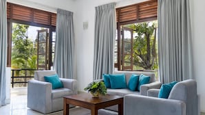 A modern living room with two grey sofas, a wooden coffee table, and a potted plant. Large windows with grey curtains provide views of greenery outside. - Villa Sarakkuwa (Negombo)