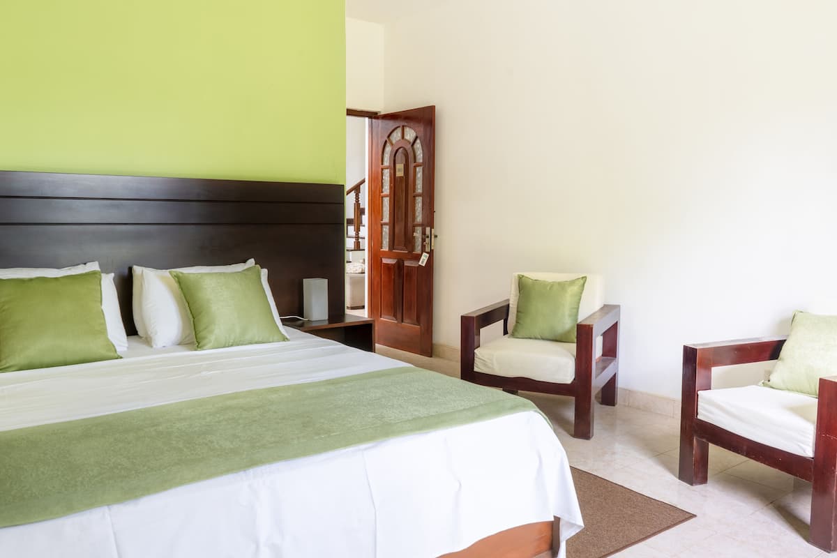 A hotel room with a large bed, two chairs, a wooden door, and a green wall.