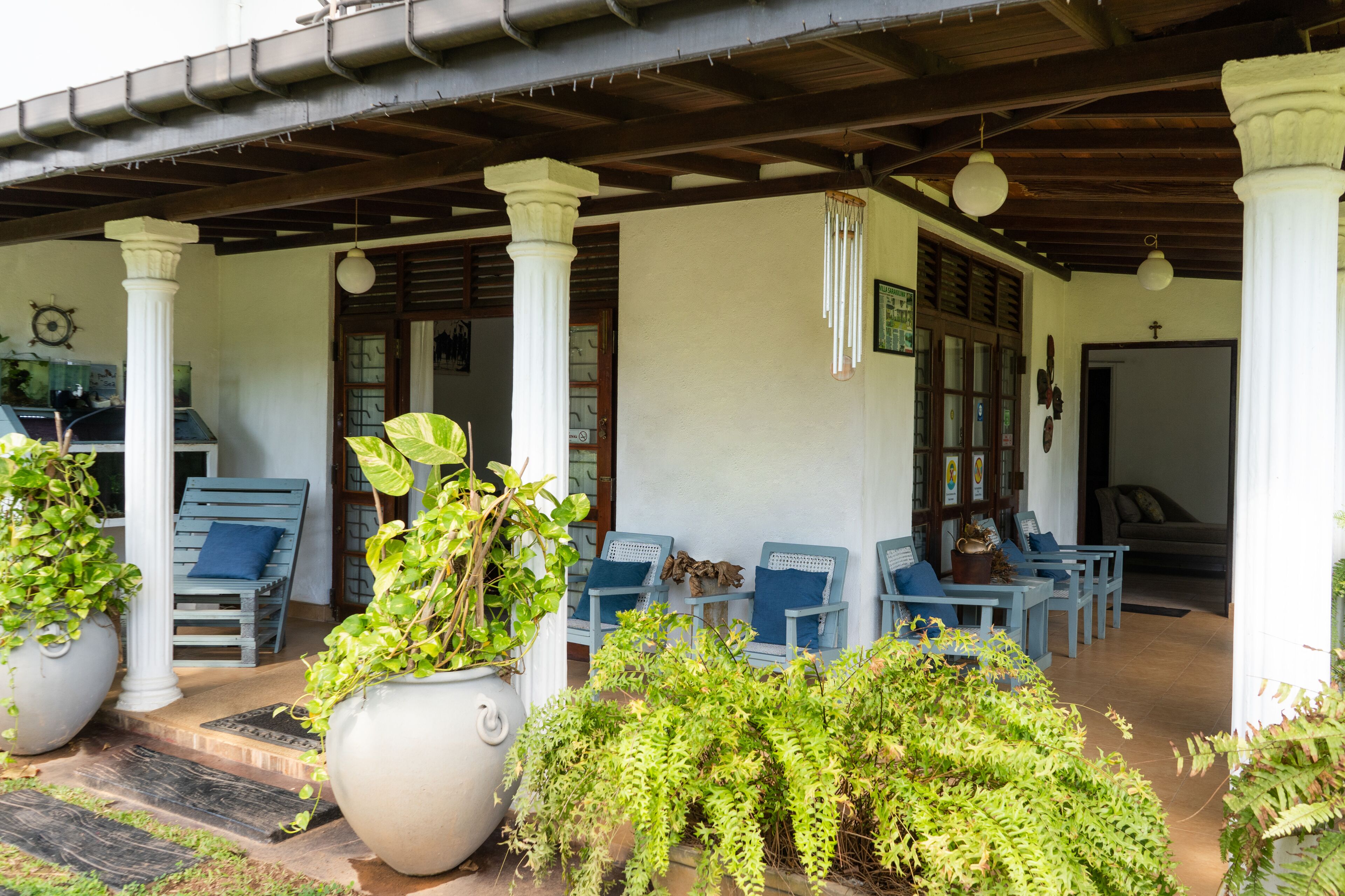 A covered outdoor seating area with white columns, blue chairs, and potted plants.