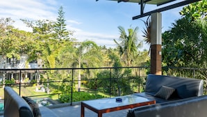 A balcony with a glass table and a sofa, overlooking a lush garden and a pool. - Villa Sarakkuwa (Negombo)