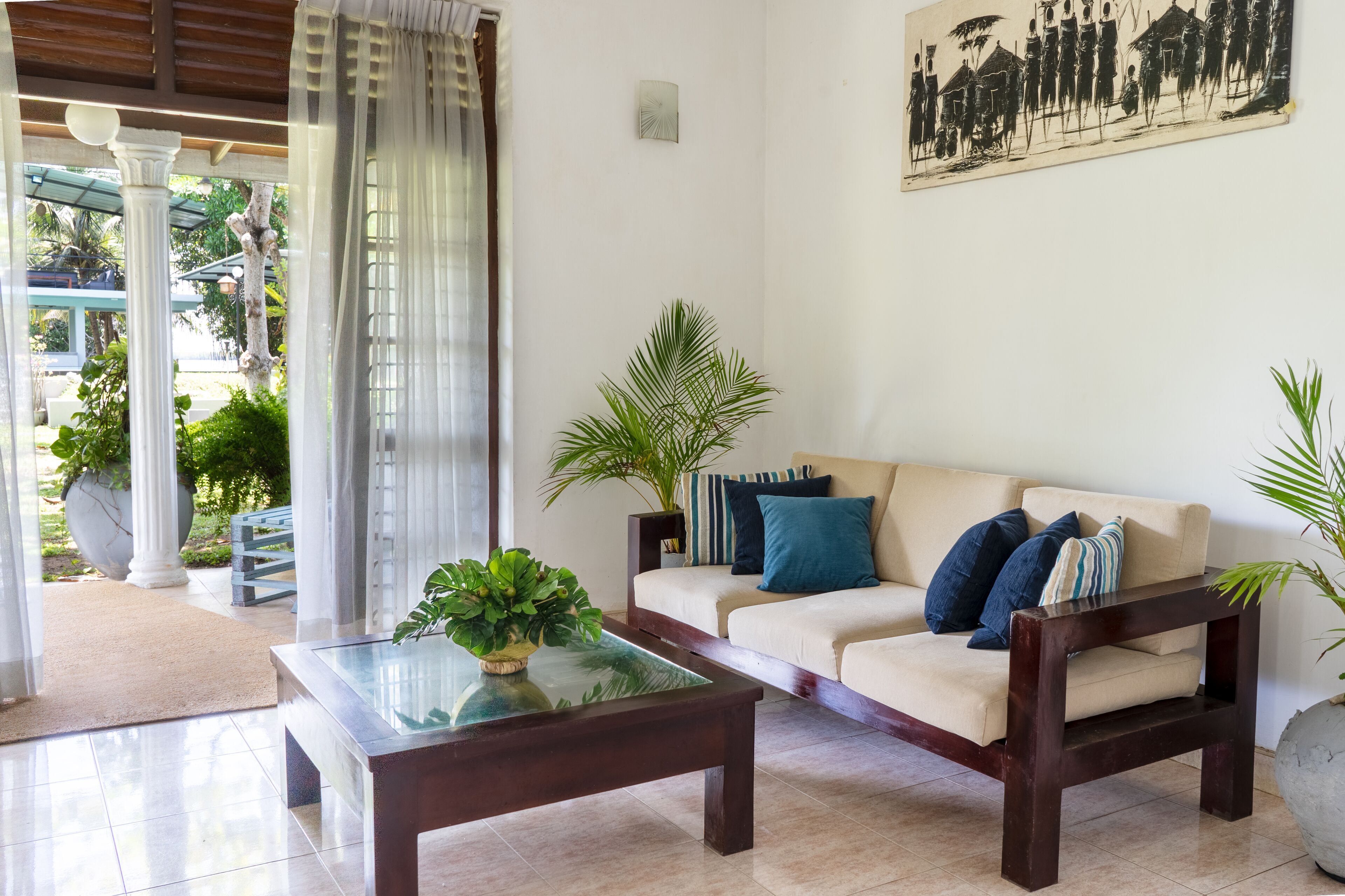 A living room with a beige sofa, dark wooden coffee table, and a glass-top table with a plant.