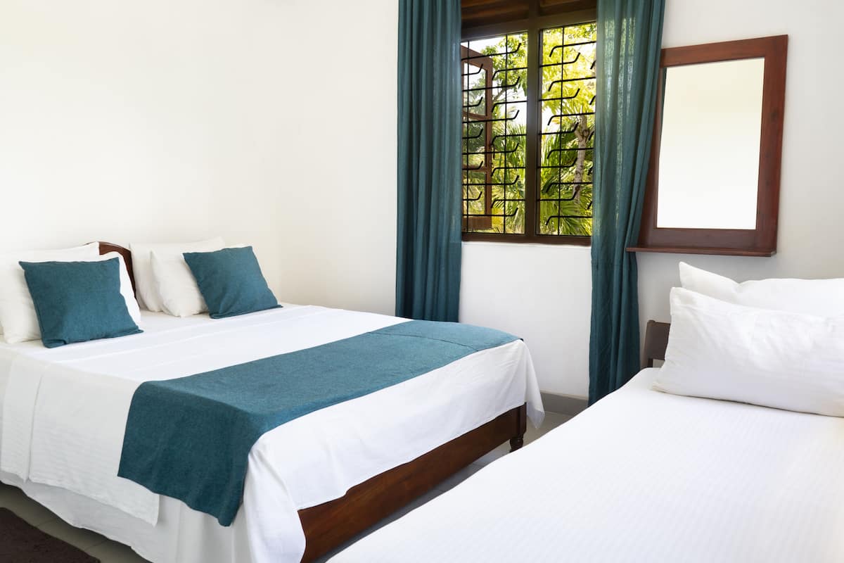 A hotel room with two beds, a window with curtains, and a mirror on the wall.