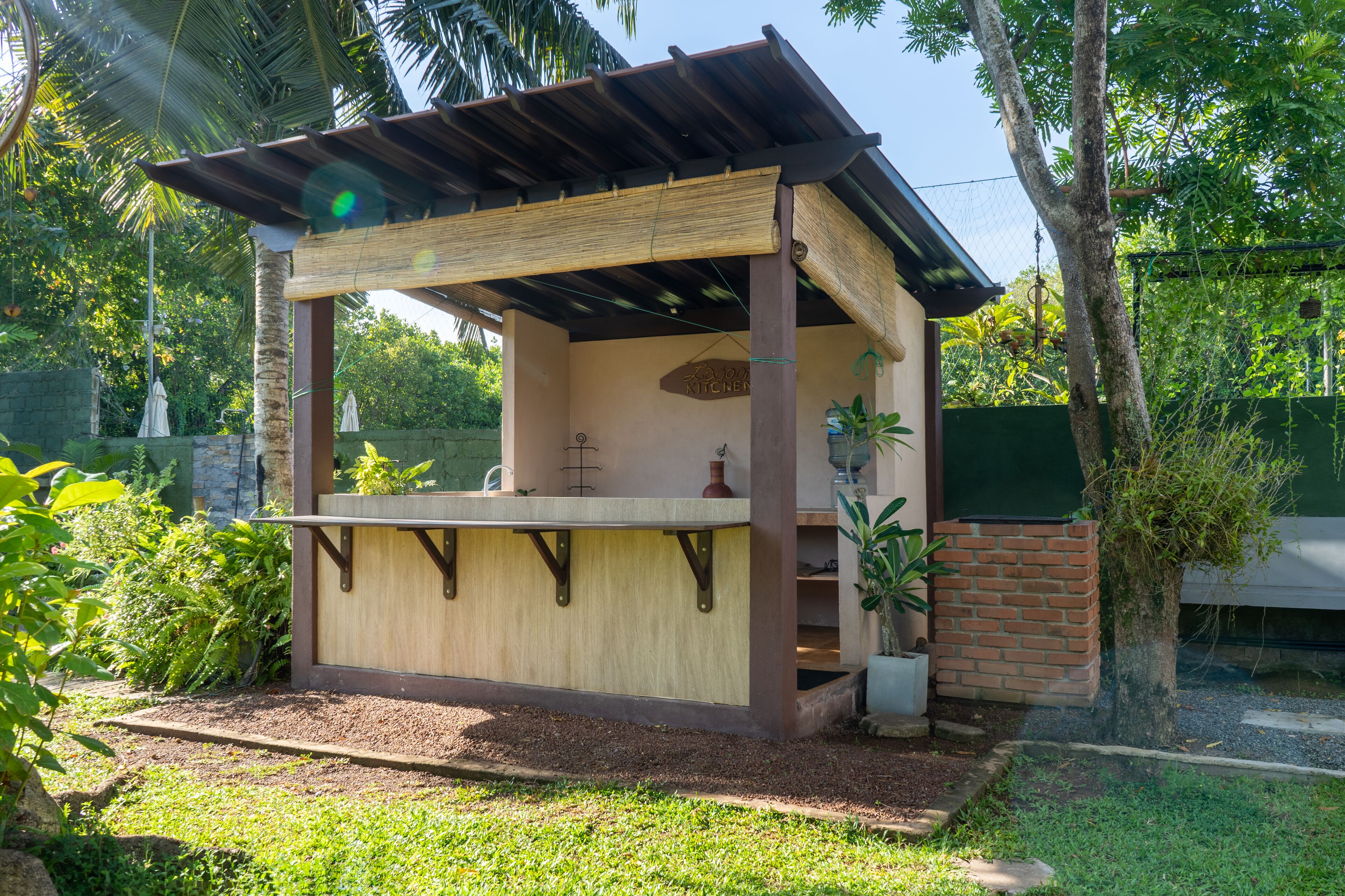 A small outdoor kitchen area with a wooden structure, a brick wall, and potted plants.