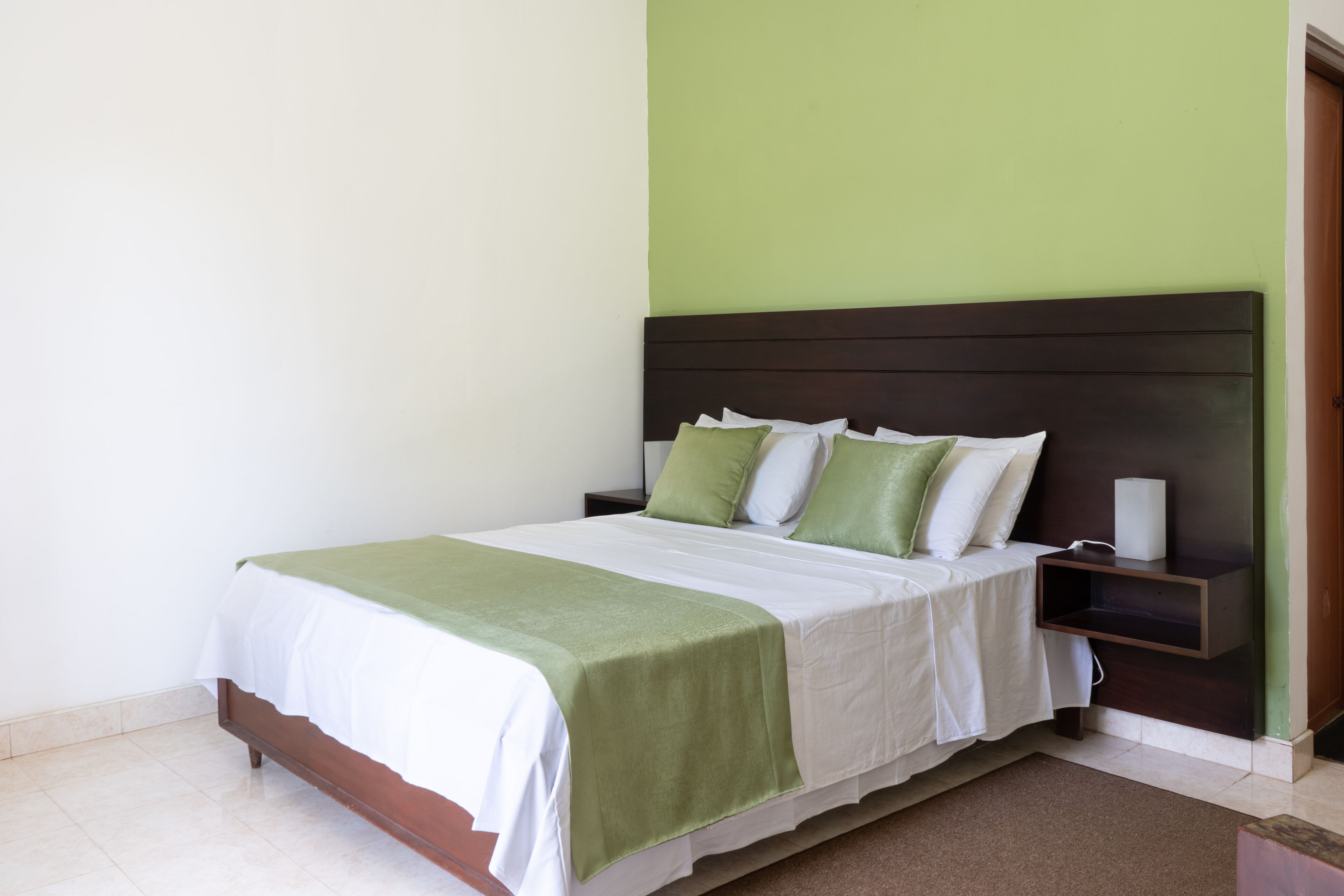 A neatly made bed with a green and white bedspread, a wooden headboard, and a bedside table with a lamp.