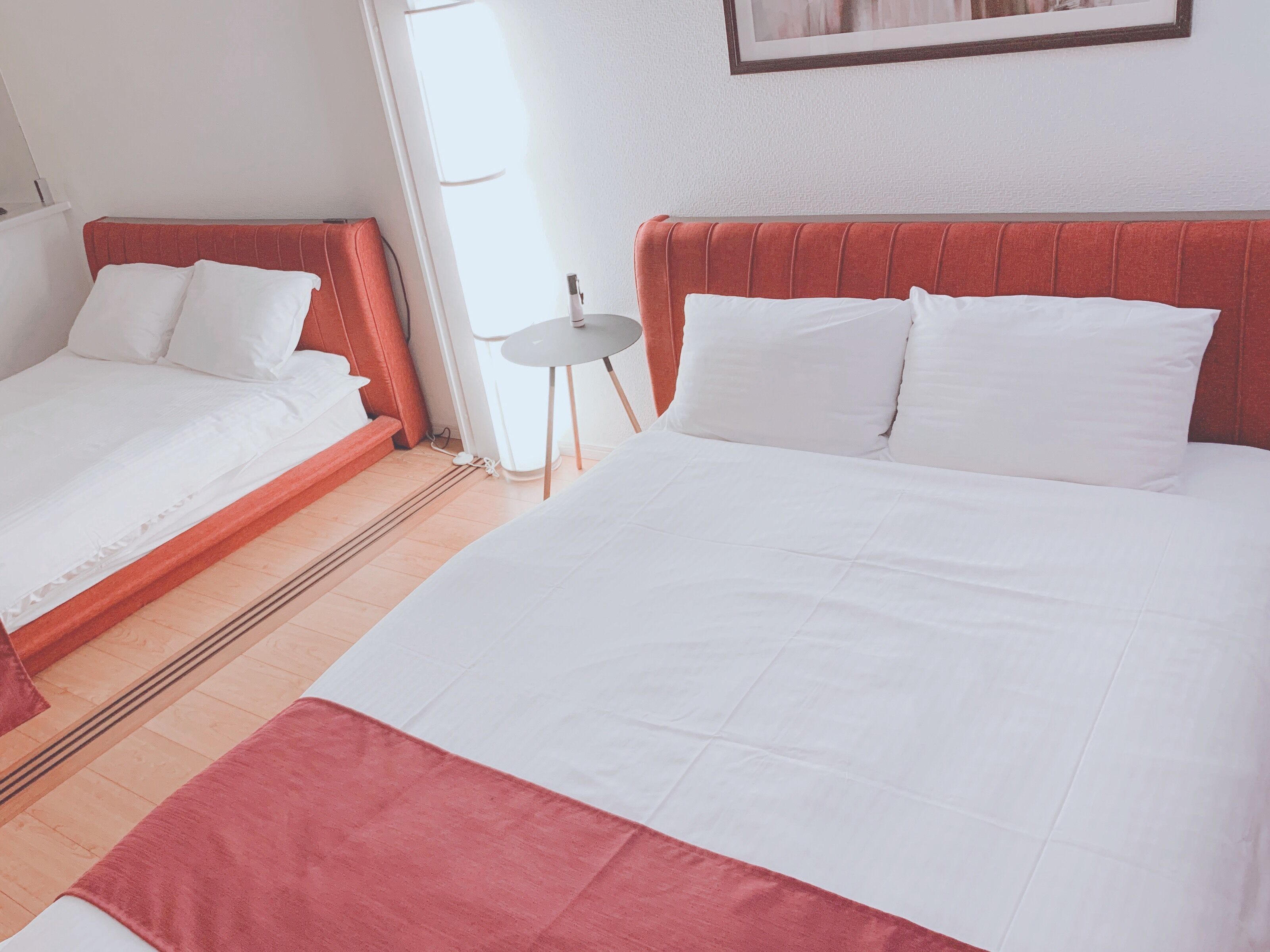 Una habitación de hotel con dos camas, una mesita y un ventanal.