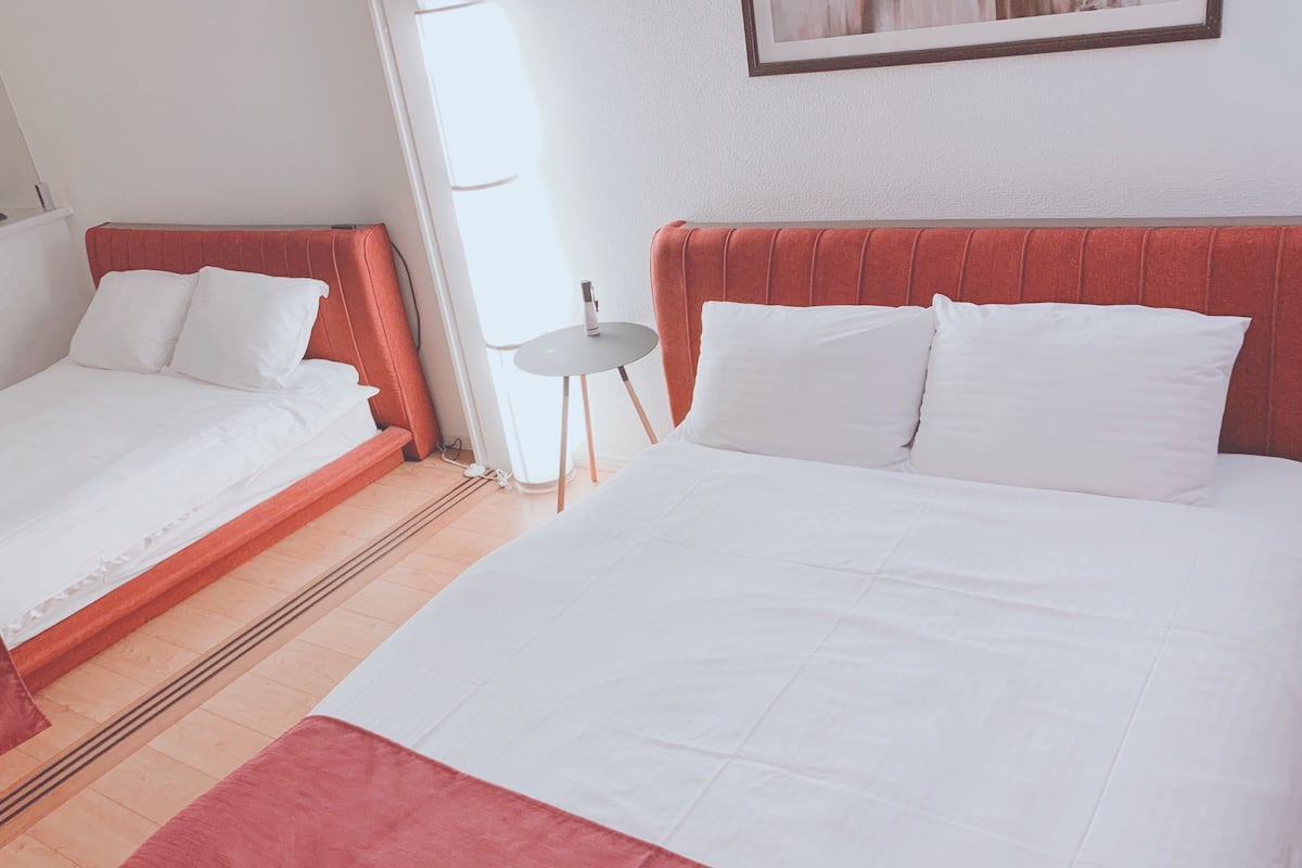 Two single beds with white linens and red headboards in a room with a tiled floor.