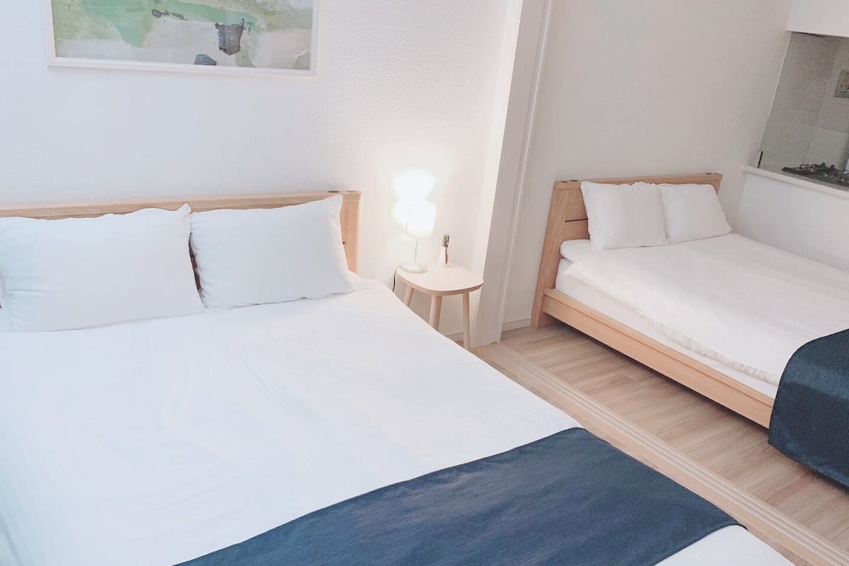 A hotel room with two beds, a small bedside table with a lamp, and a wall-mounted artwork.
