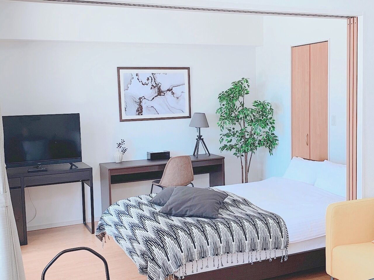 Un dormitorio con cama, escritorio, televisor, lámpara y planta.