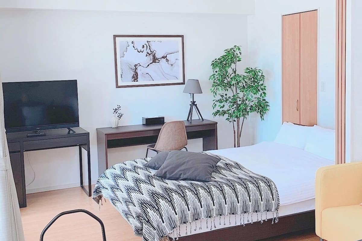 A bedroom with a bed, a desk, a TV, a lamp, and a plant.