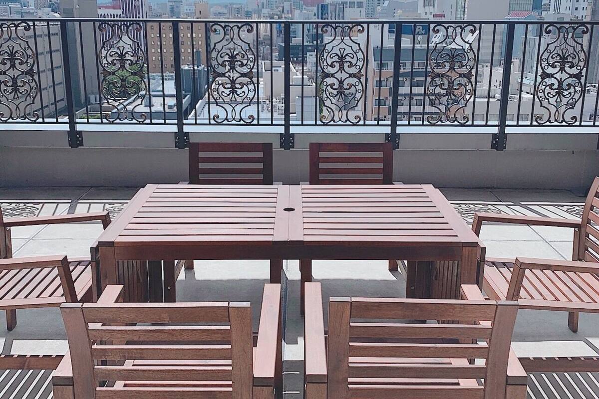 Una terraza en la azotea con mesa y sillas de madera, barandilla metálica decorativa y vista panorámica de la ciudad.