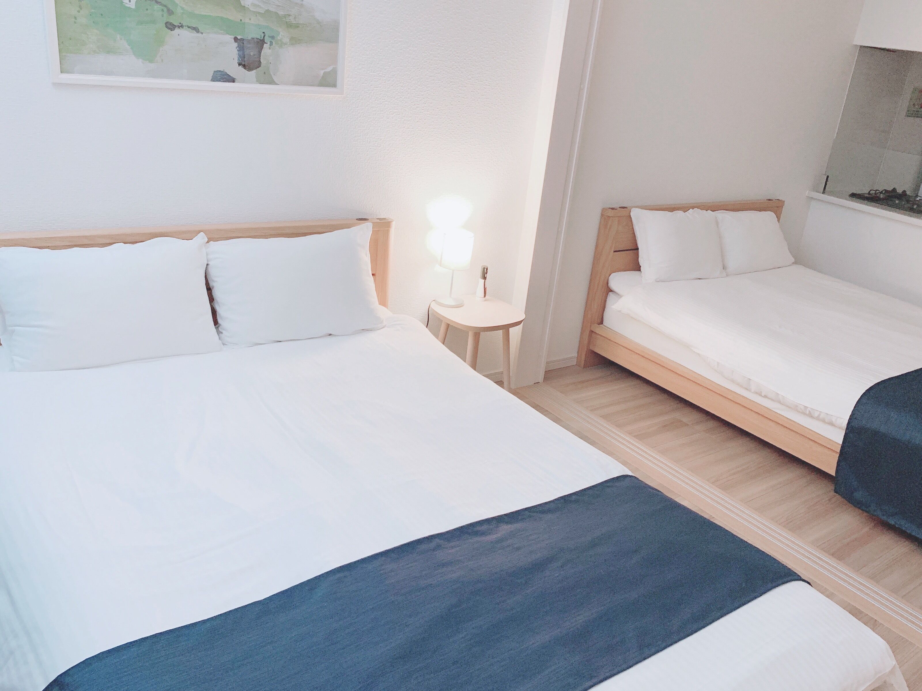 Habitación de hotel con dos camas, una mesita de noche con lámpara y un cuadro en la pared.