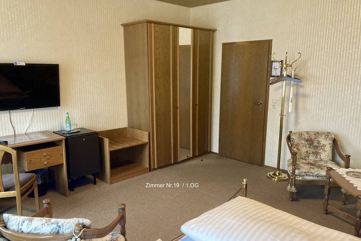 A hotel room with a bed, a desk, a wardrobe, a chair, and a television.