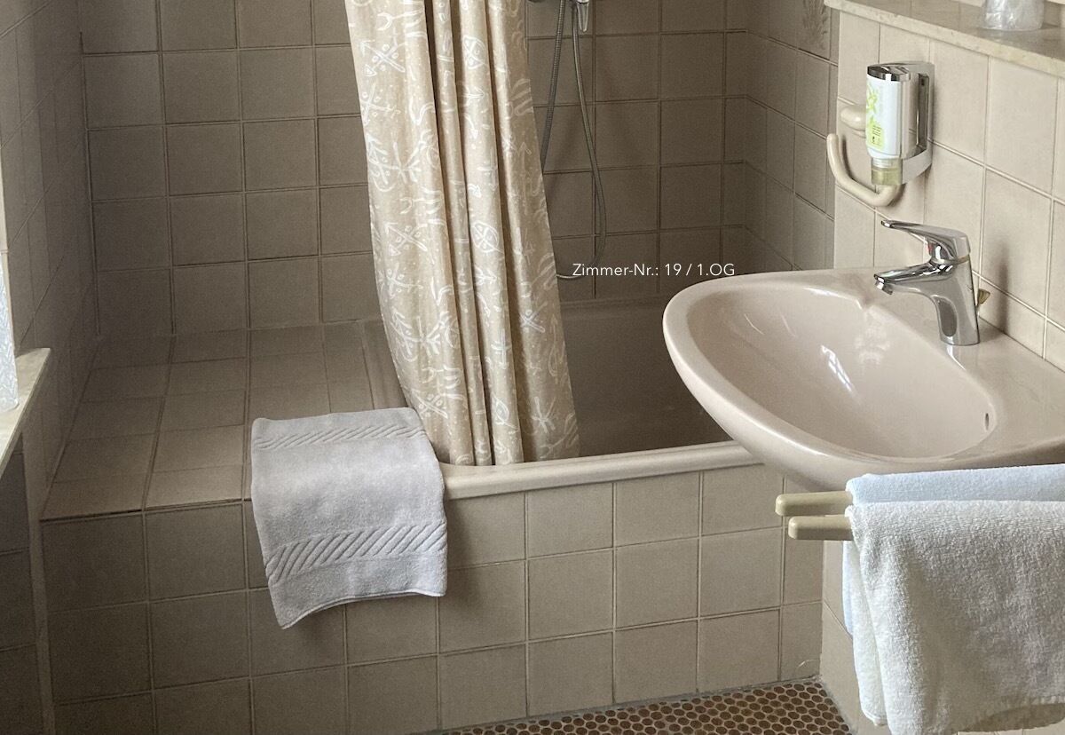 Ein Badezimmer mit Badewanne, Waschbecken und Dusche. Eine Handtuchstange mit Handtüchern und einer Seifenspende an der Wand.