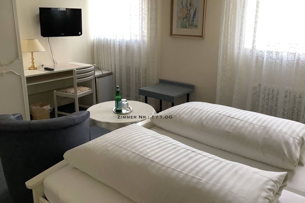 A hotel room with two beds, a desk, a chair, a TV, and a painting on the wall.