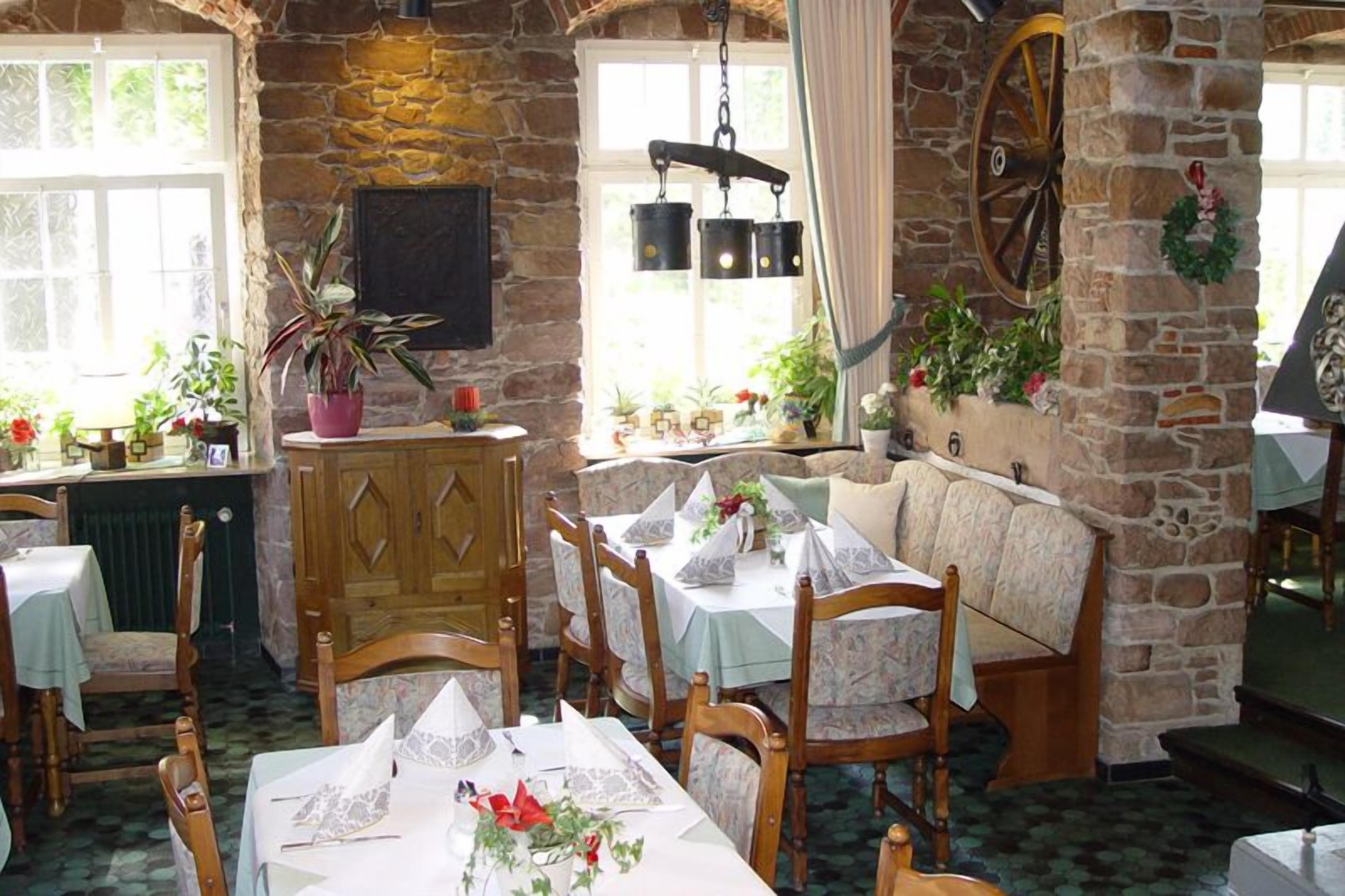 Un accogliente ristorante con pareti in pietra, arredi in legno e diverse piante. I tavoli sono apparecchiati con tovaglie e tovaglioli bianchi.