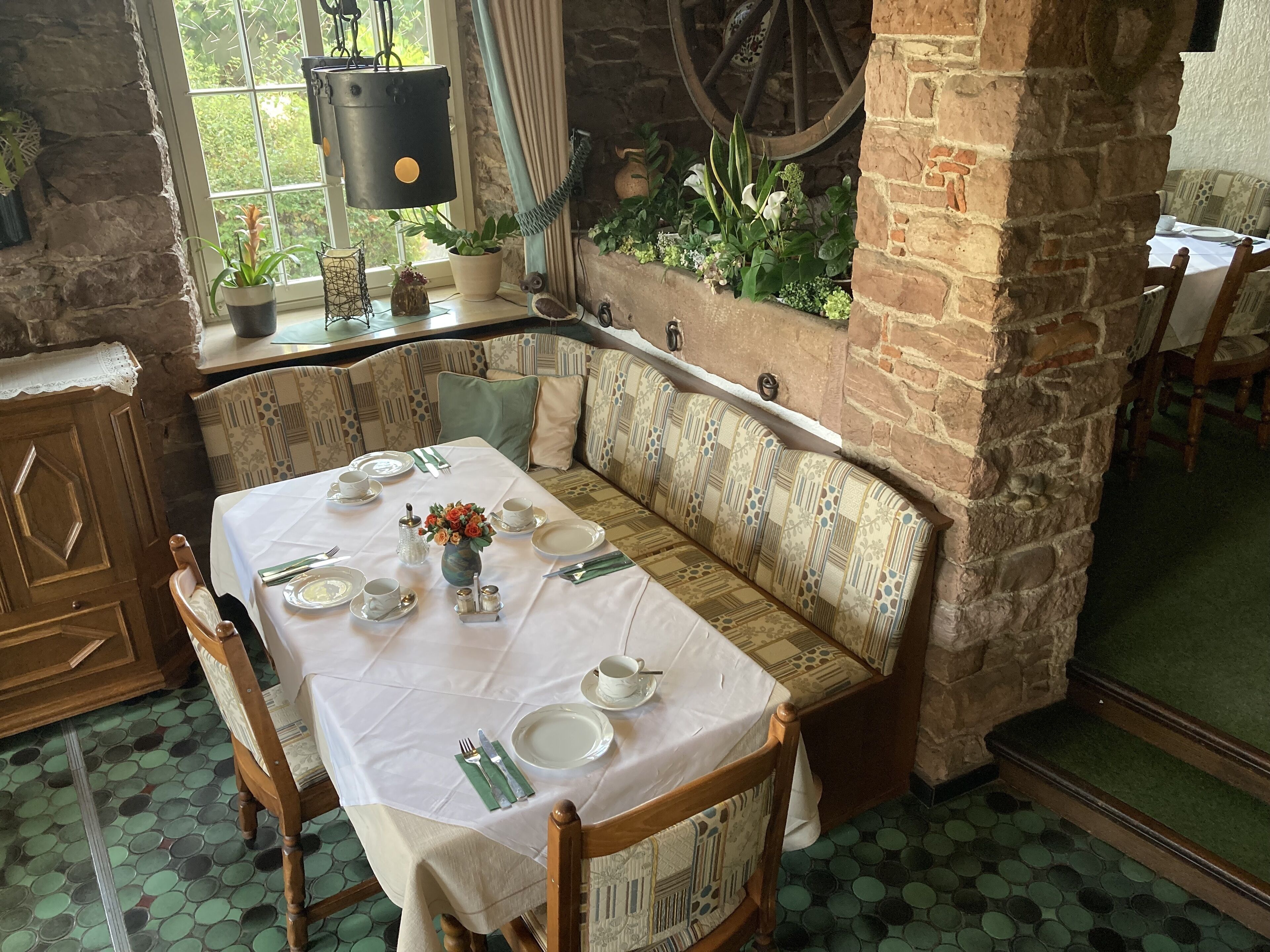 A cozy dining area with a table set for two, a bench, and a rustic stone wall.