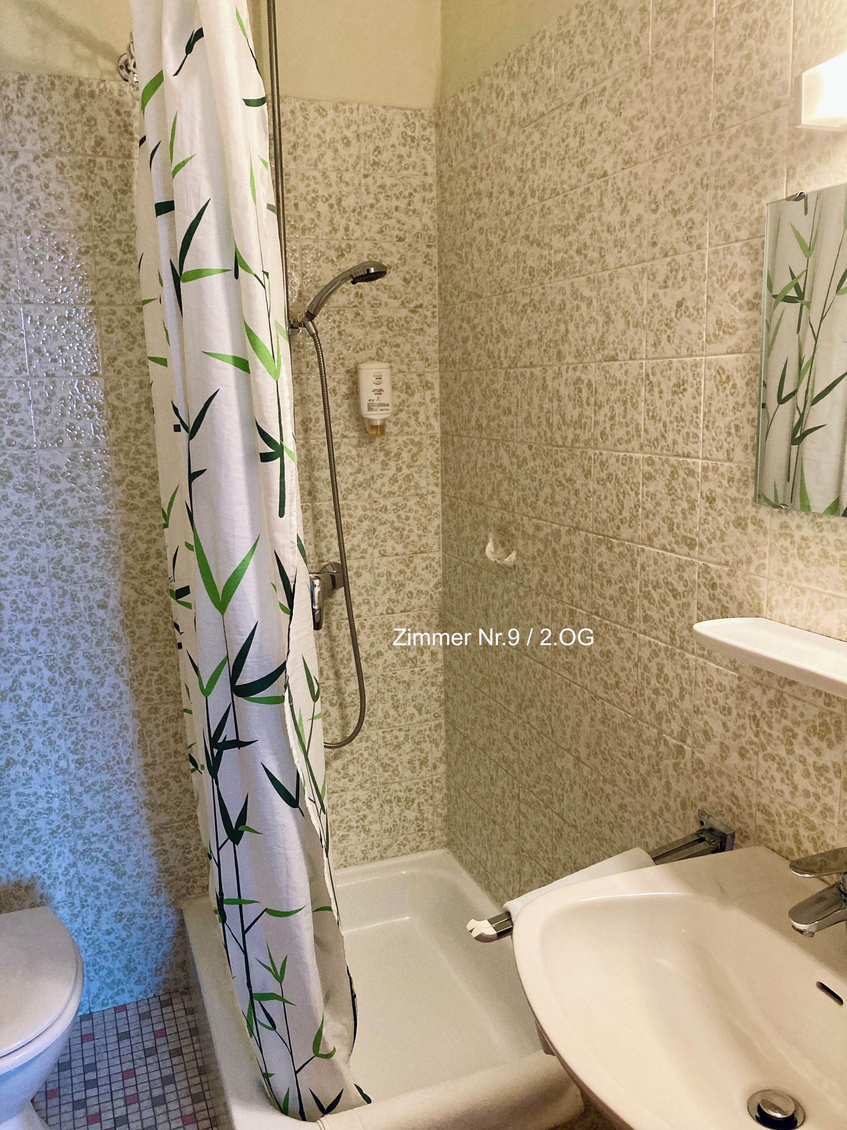 Un baño con cortina de ducha con estampado de bambú, una bañera, un inodoro y un lavabo con espejo.